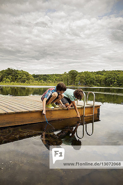 Junge zeigt auf Wasser  während er mit seinem Bruder am Dock fischt