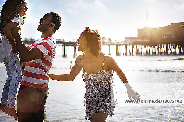 Frau betrachtet Mann  der seine Tochter trägt  während sie sich am Strand vergnügt