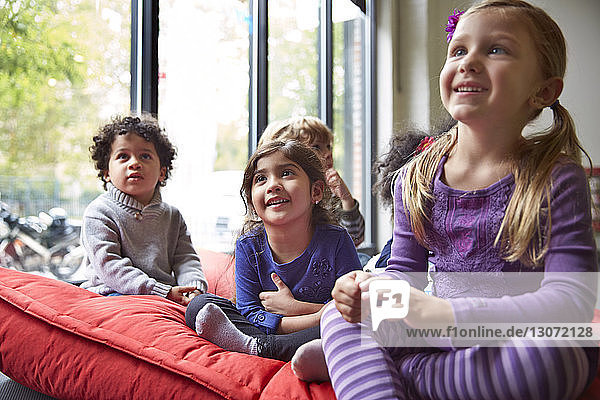 Lächelnde Kinder entspannen sich in der Vorschule auf einer Decke am Fenster
