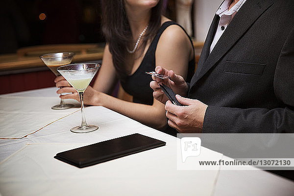 Mittendrin ein Mann  der eine Kreditkarte hält  während er mit seiner Freundin im Restaurant sitzt