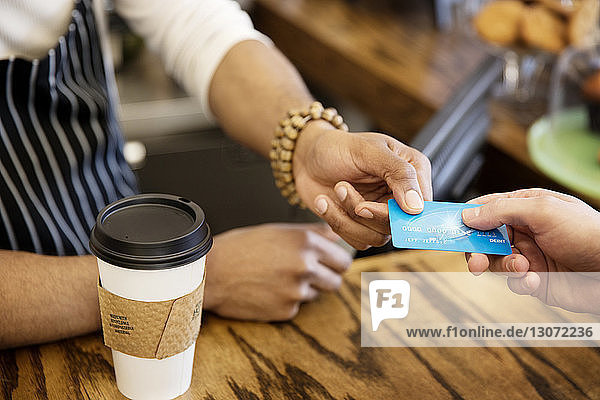 Schrägaufnahme eines Mannes  der dem Besitzer im Café eine Debitkarte gibt