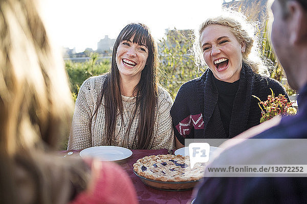 Fröhliche Frauen lachen  wenn sie während der Party mit Freunden an einem Tisch im Freien sitzen