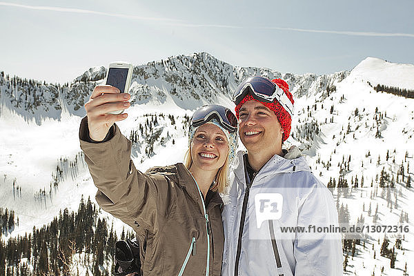 Couple taking selfie while standing on snow covered mountain