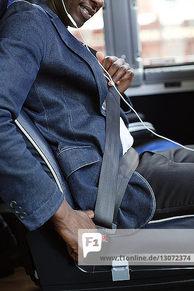 Cropped image of man adjusting seat belt while sitting in bus