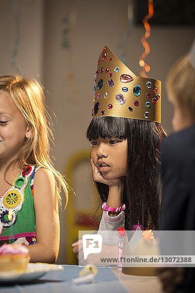 Mädchen mit Hand am Kinn schaut sich während der Geburtstagsfeier Cupcake an