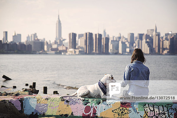 Frau sitzt mit Hund auf mehrfarbiger Stützmauer am Meer gegen die Stadt