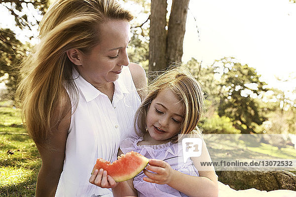 Mutter betrachtet Mädchen mit Wassermelone im Garten