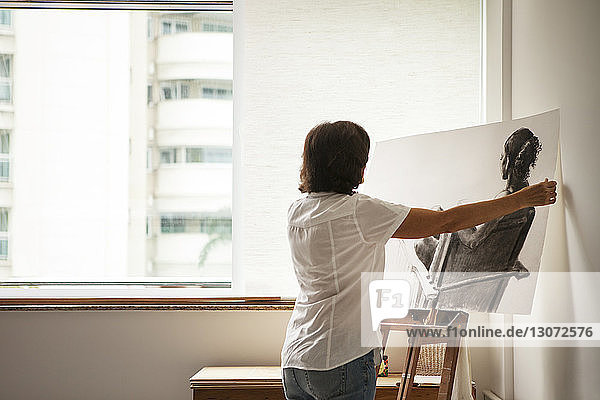 Rückansicht einer Frau  die im Kunstatelier ein Gemälde auf die Staffelei stellt