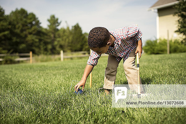 Boy playing croquet while standing on grassy field in backyard