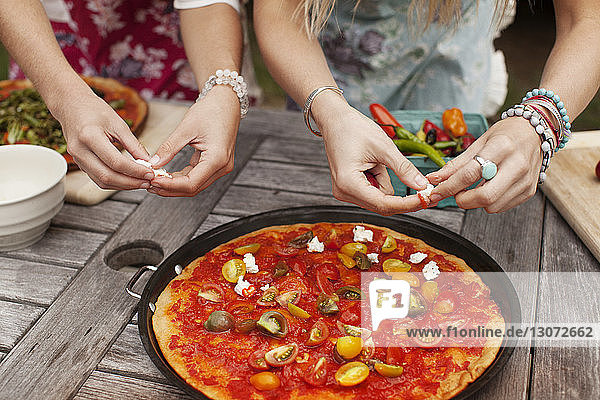 Mitsektion von Freunden beim Belag auf Pizza