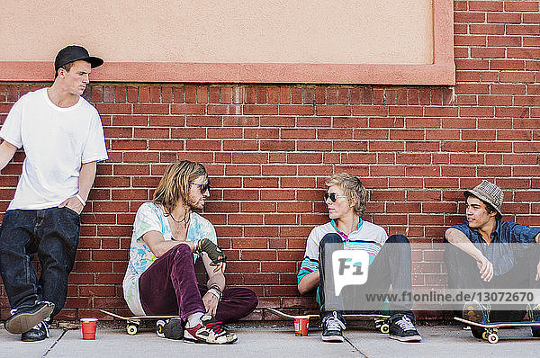 Freunde mit Skateboard reden  während sie an einer Ziegelmauer sitzen