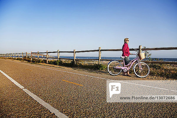 Frau mit Fahrrad schaut weg  während sie gegen das Meer steht