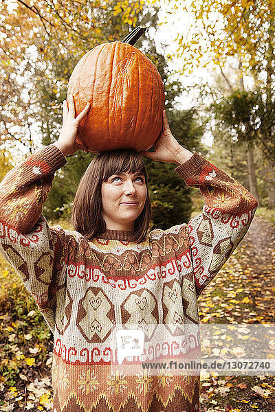 Frau schaut auf  während sie einen Halloween-Kürbis trägt
