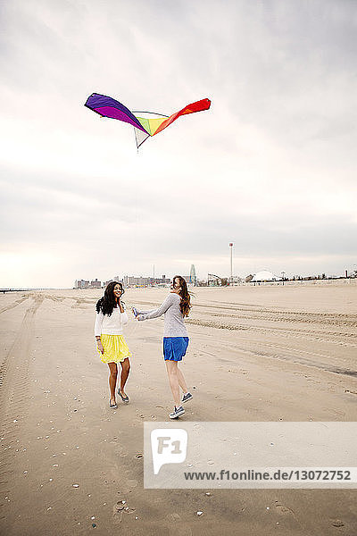 Teenager looking at friend flying kite against sky