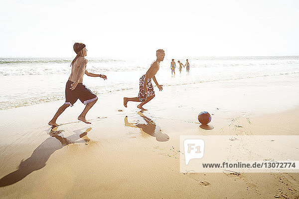 Side view of boys playing soccer on beach against clear sky