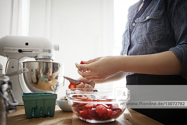 Mittelsektion einer Frau  die Erdbeeren schneidet  während sie zu Hause an der Küchentheke steht