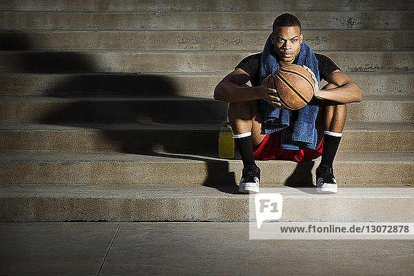 Portrait of athlete with basketball sitting on steps