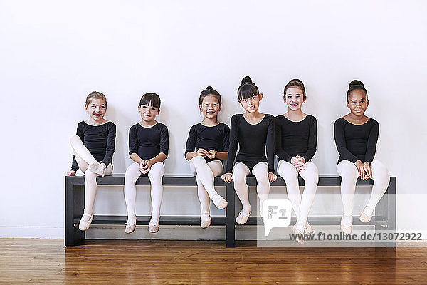 Portrait of confident ballerinas sitting on bench at ballet studio