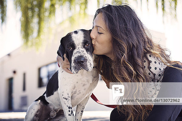 Liebende Frau küsst Hund gegen Gebäude