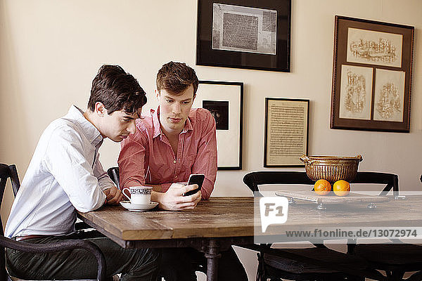 Schwule Männer  die am Tisch sitzend auf ein Smartphone schauen