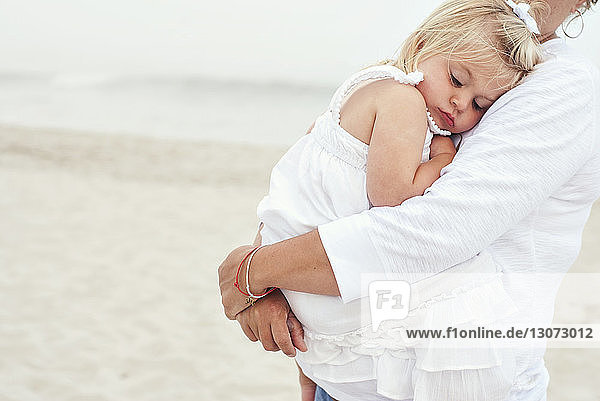 Midsection of mother carrying girl while standing at beach