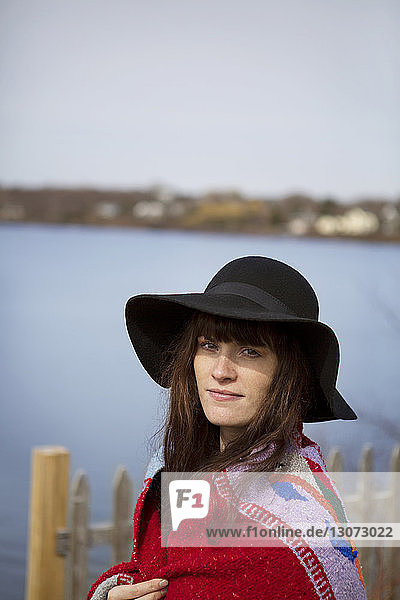 Porträt einer lächelnden Frau mit Hut in Decke gehüllt am See stehend