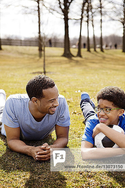 Vater und Sohn mit Fussball auf dem Spielfeld im Park liegend