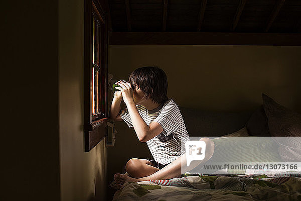 Boy looking through binoculars while sitting on bed in cabin
