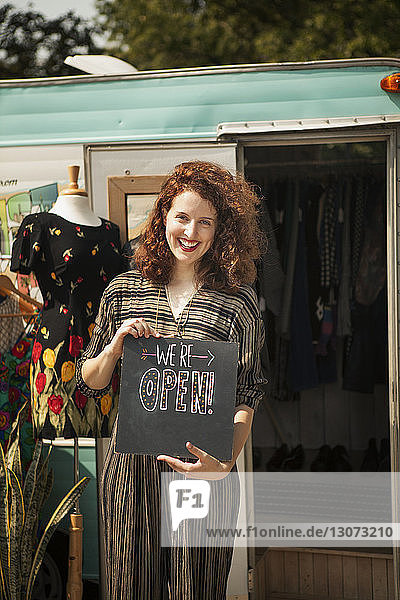 Porträt einer lächelnden Frau mit Eröffnungsbrett  die gegen ein Wohnmobil steht