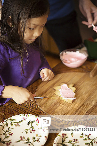 Hochwinkelaufnahme eines Mädchens  das Creme auf einen Keks aufträgt