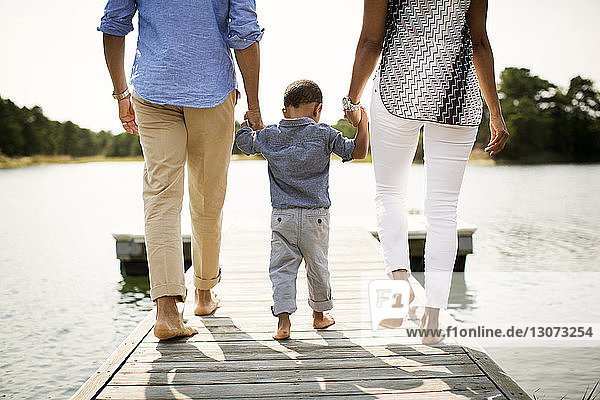 Low section of parents holding son's hands while walking on pier