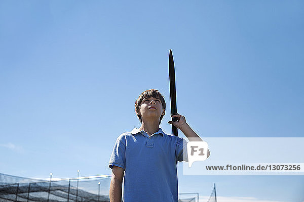 Niedrigwinkelansicht eines Jungen  der eine Rakete hält  während er vor einem klaren blauen Himmel steht