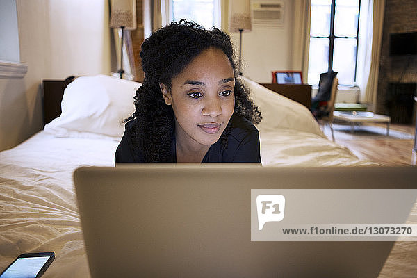 Woman using laptop computer while lying on bed