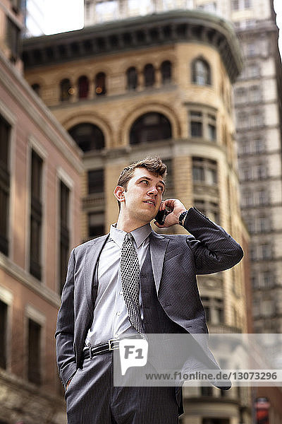 Businessman talking on smart phone while standing against buildings in city