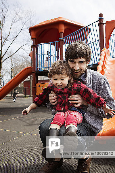 Porträt eines Mannes mit Tochter am Spielplatz kauernd