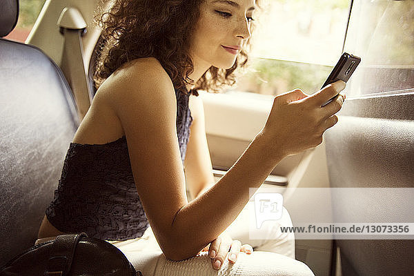 Seitenansicht einer Frau  die während einer Autofahrt ein Smartphone benutzt