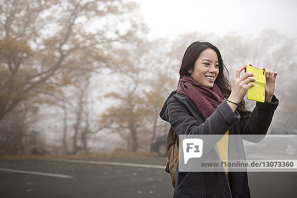 Frau fotografiert durch Mobiltelefon  während sie auf der Straße steht