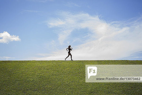 Sportler joggt auf grasbewachsenem Feld vor bewölktem Himmel