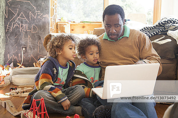 Father showing laptop computer to children while sitting on floor at home