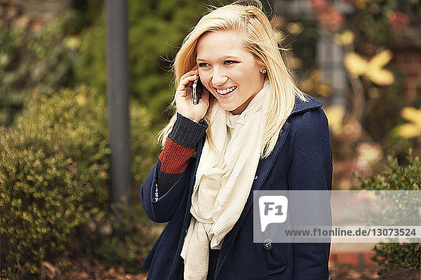 Cheerful woman talking on phone while standing at park during winter