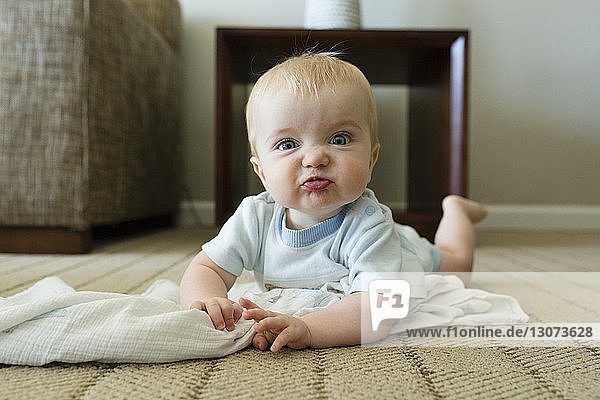 Porträt eines süßen  verspielten Jungen  der ein Gesicht macht  während er zu Hause auf dem Teppich liegt
