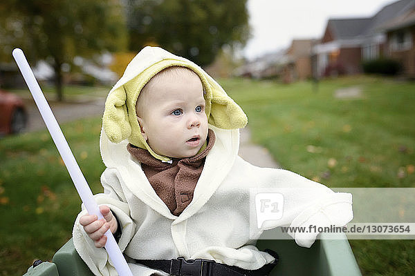 Boy with stick looking away while sitting in baby carriage