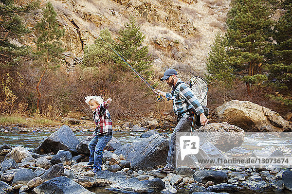 Father and son walking on rocks amidst river by mountain
