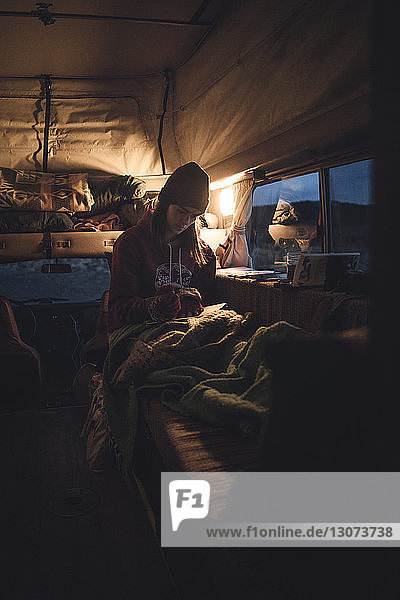 Woman reading book while sitting in camper van during sunset