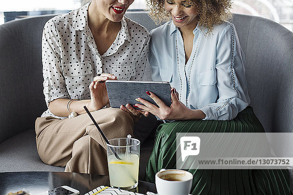 Midsection of female colleagues using tablet computer while sitting on sofa at cafe