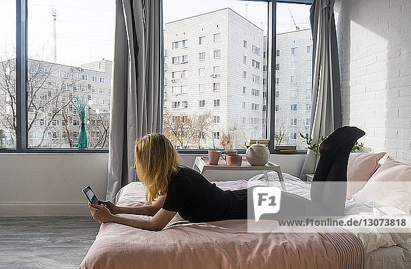 Frau benutzt Tablet-Computer  während sie zu Hause im Bett liegt