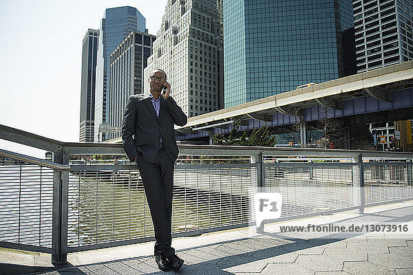 Businessman leaning on railing and talking on mobile phone against buildings