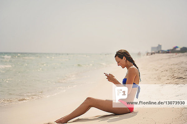 Glückliche Frau telefoniert  während sie sich am Strand vor klarem Himmel entspannt