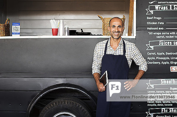 Portrait of confident male owner holding tablet computer while standing against food truck