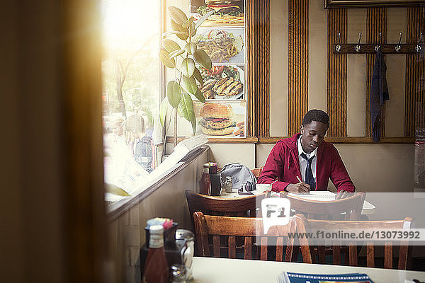 Teenager in school uniform writing while sitting at restaurant